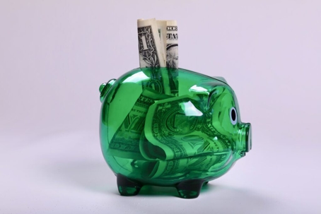 A green transparent piggy bank with bills inside